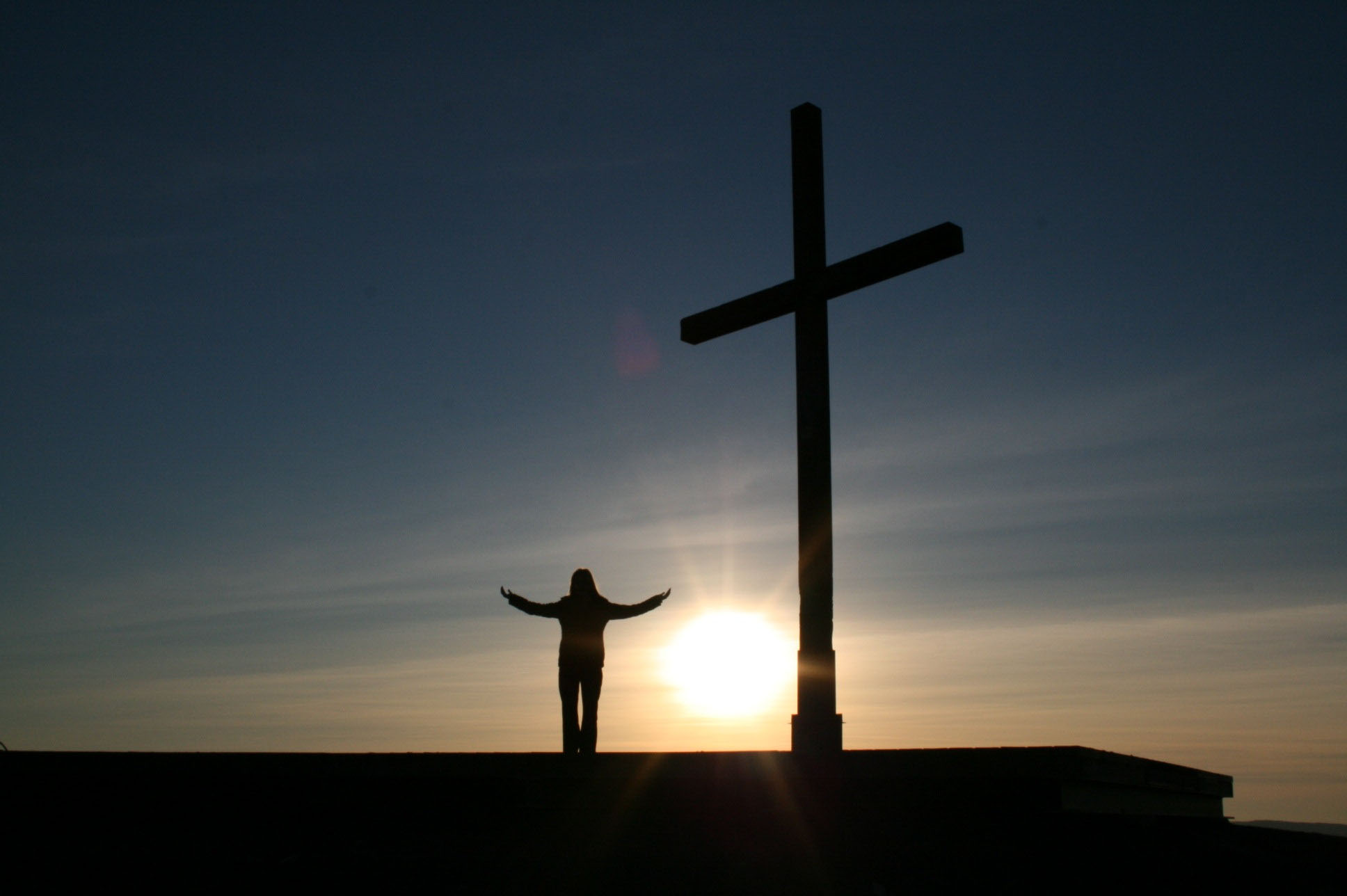 Kreuz und Mensch stehen auf einem Berg vor einem Sonnenaufgang