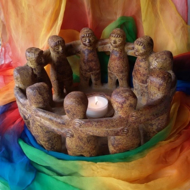 Tonskulptur-12 Personen stehen im Kreis und halten sich an den Händen, in der Mitte eine Kerze