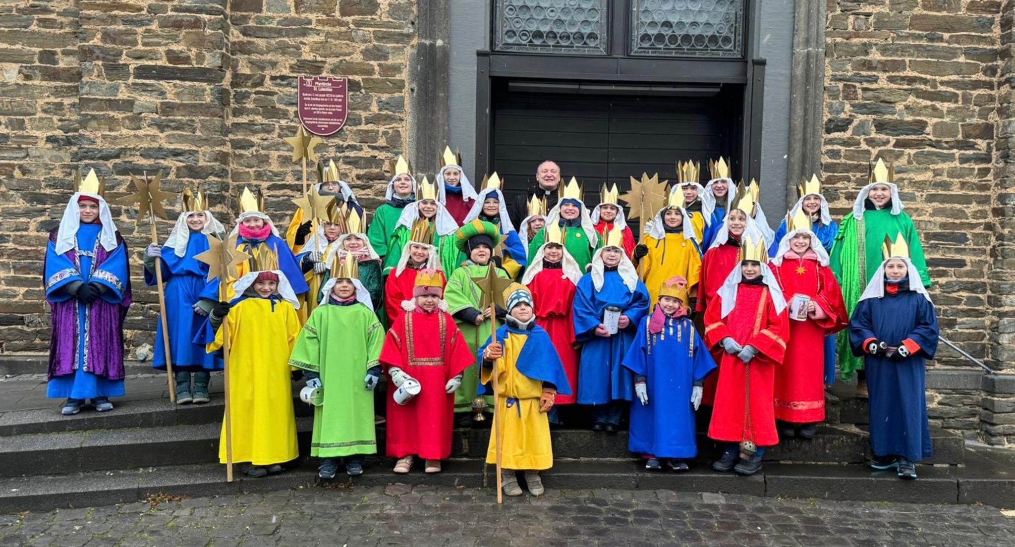 Die diesjährigen Sternsinger haben sich nach der Aussendung mit Pfarrer Konrad Lisowski auf den Treppenstufen vor der Pfarrkirche versammelöt.